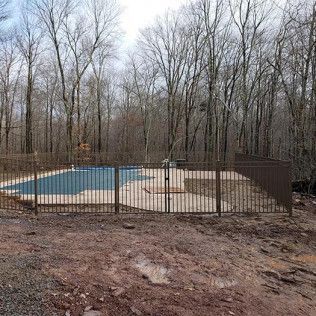 Brown fenced in-ground pool in a wooded area, surrounded by bare trees.