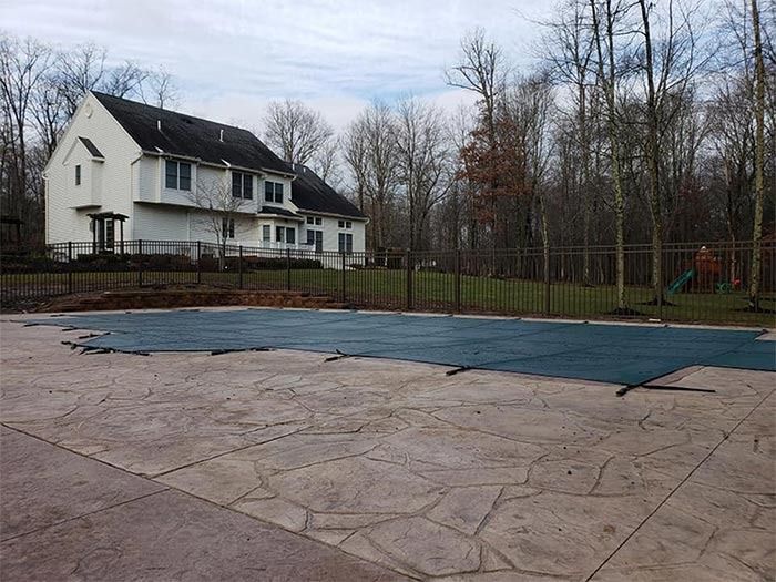 A large house with a pool covered for the season. Trees in the background. Overcast sky.