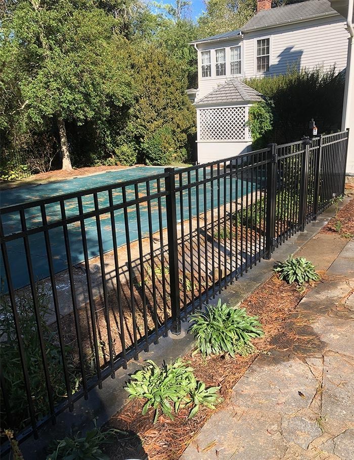 Black metal fence surrounding a pool with a blue cover, near a house with white siding.