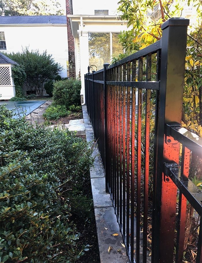 Black metal fence along a stone wall and landscaping beside a house.