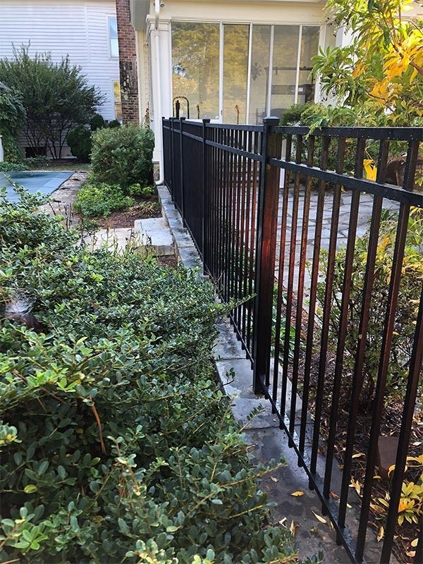 Black metal fence bordering a small garden with green bushes, next to a building.
