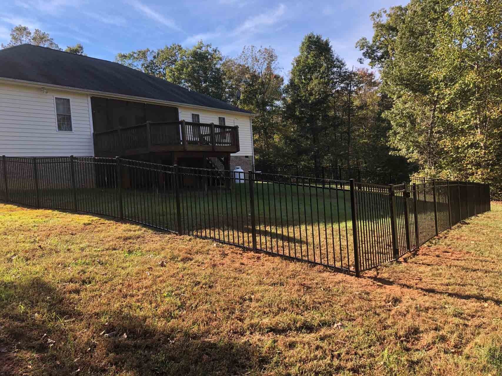 Black mesh fence encloses a grassy backyard next to a two-story house with a screened porch.