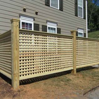 Wooden lattice fence next to a building with windows and dark shutters; brown and tan colors.