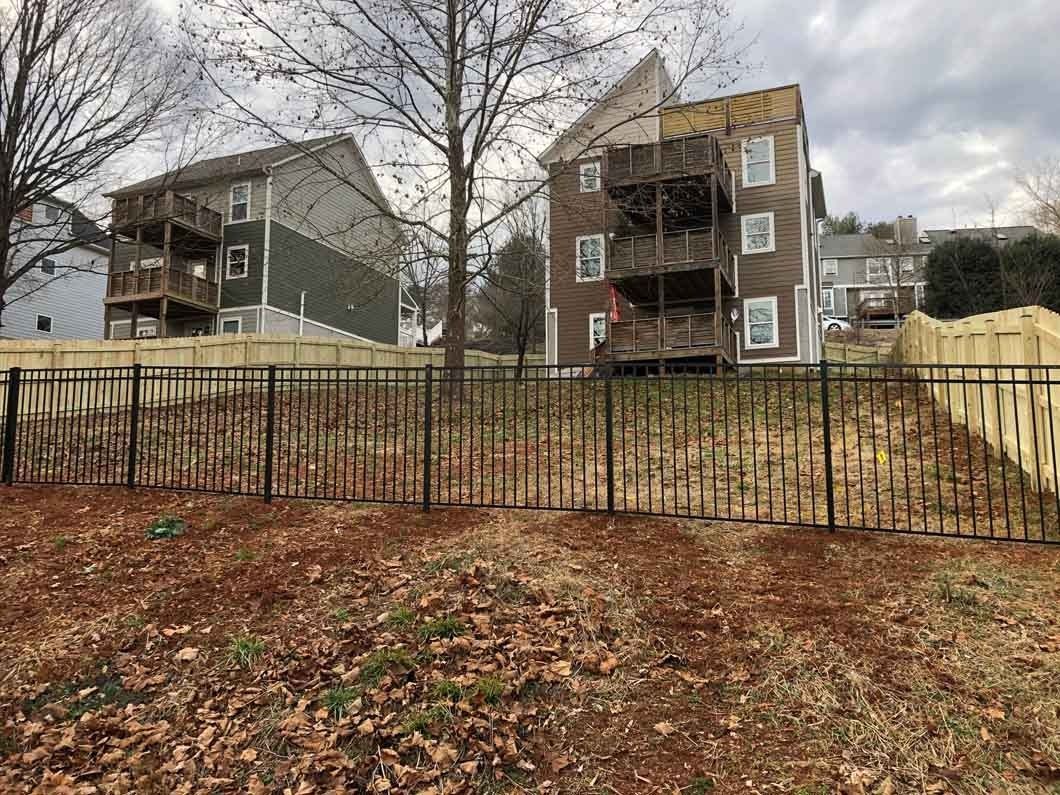 Two-story homes with balconies behind a black metal fence on a hillside, with bare trees and brown grass.