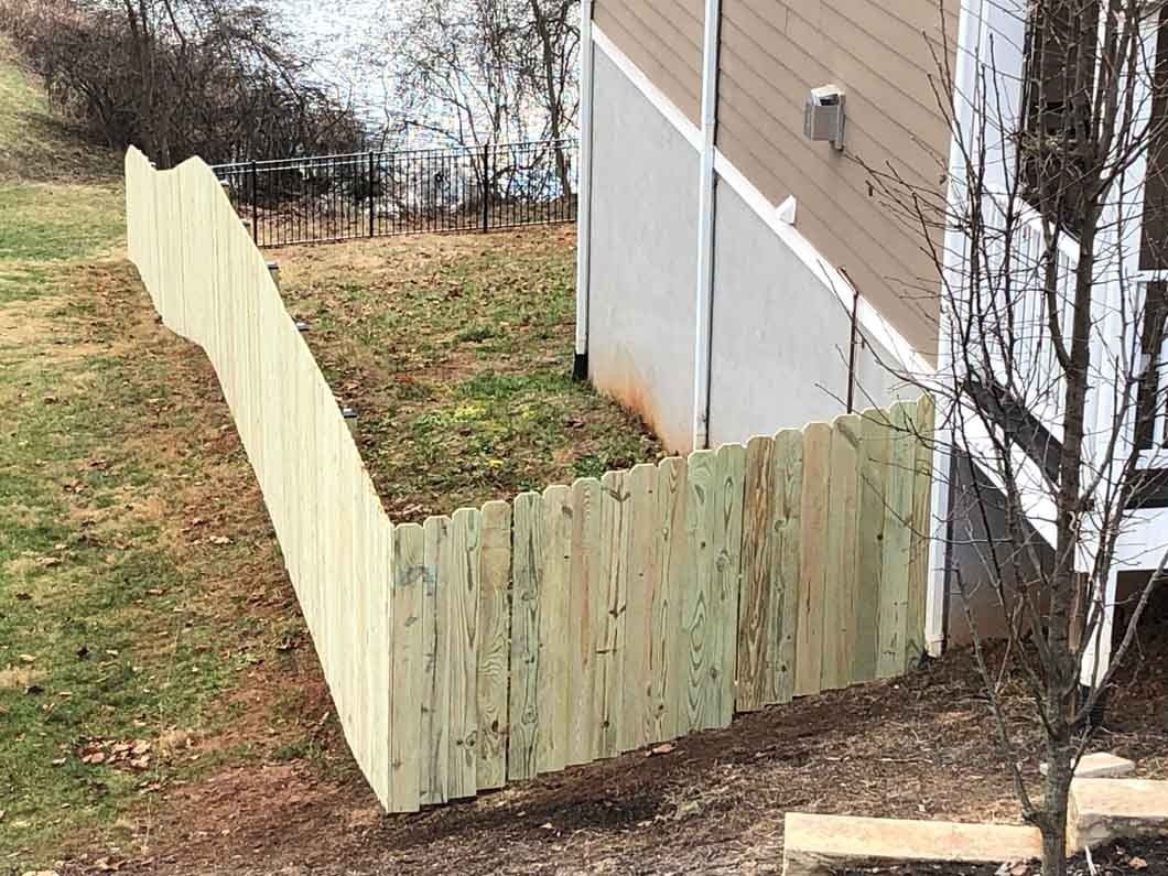 Wooden fence enclosing a grassy yard next to a light-colored building.
