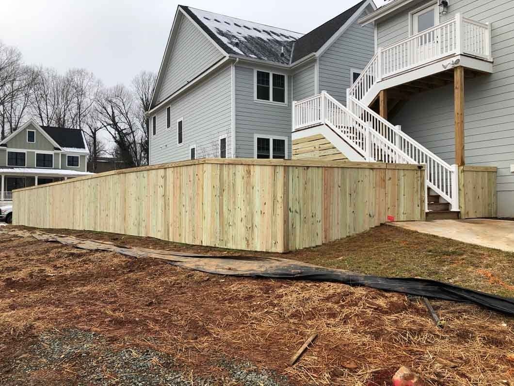 Wooden fence in front of a gray house, with a set of stairs on the right. Overcast day.
