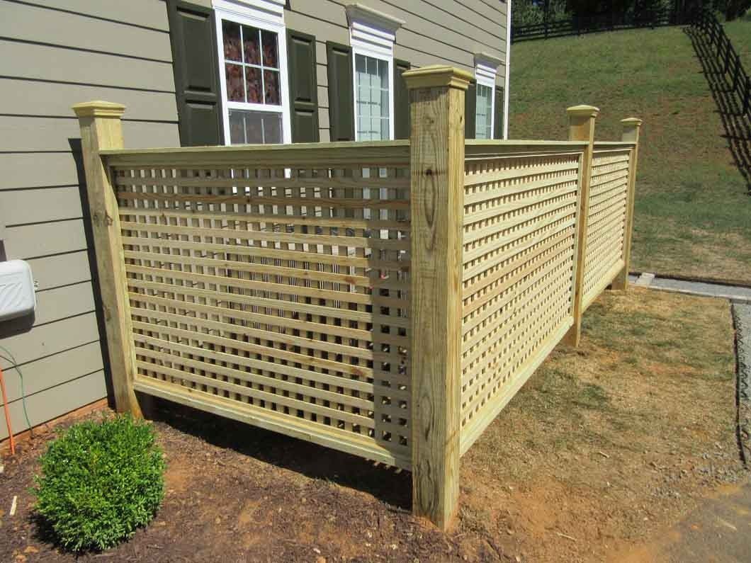 Wooden lattice fence in front of a building, next to a small green bush.