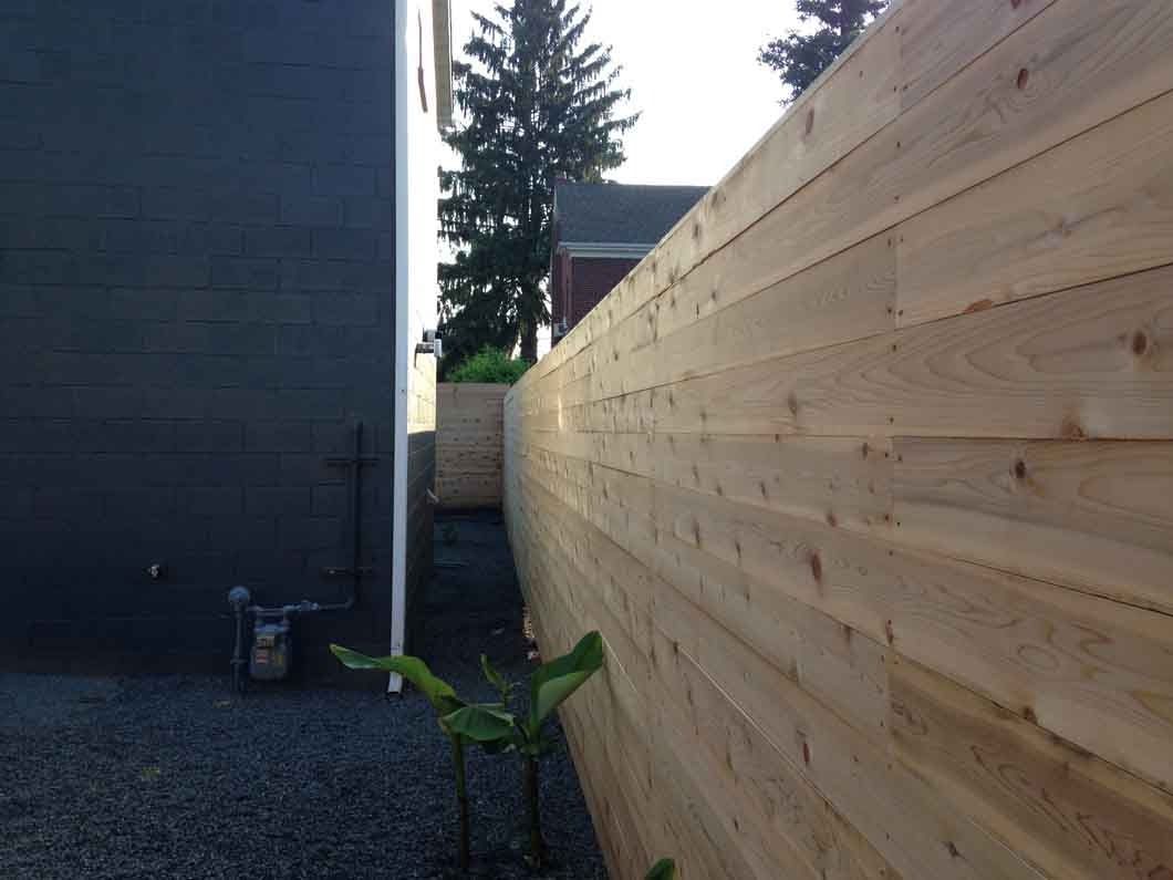 Wooden fence running along a dark gray building and gravel ground.
