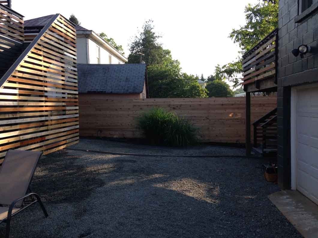 Gravel backyard with wooden fence and siding. A chair sits on the left, next to a building with unique wood paneling.