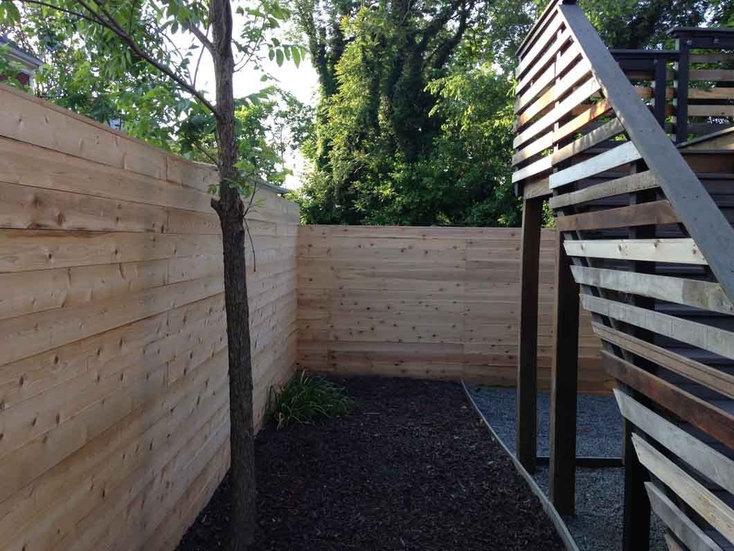 Wooden fence encloses a small yard with dark mulch and a tree. A play structure's corner is visible.