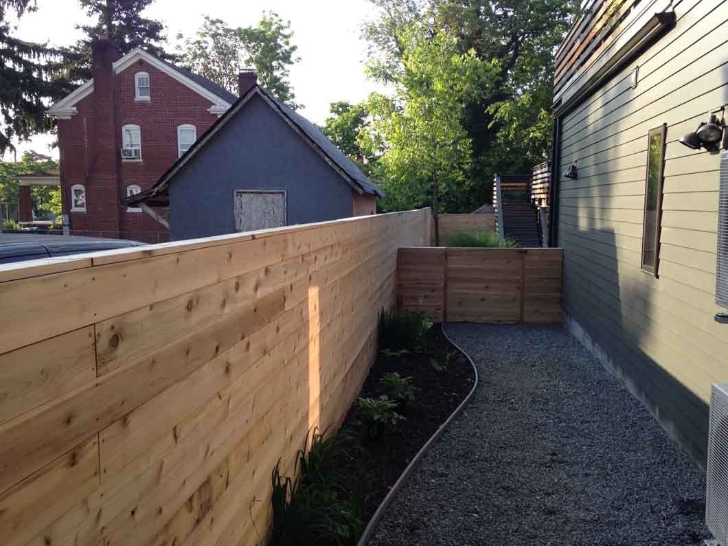 Wooden fence along a gravel path with a small garden bed and a blue shed in the background.