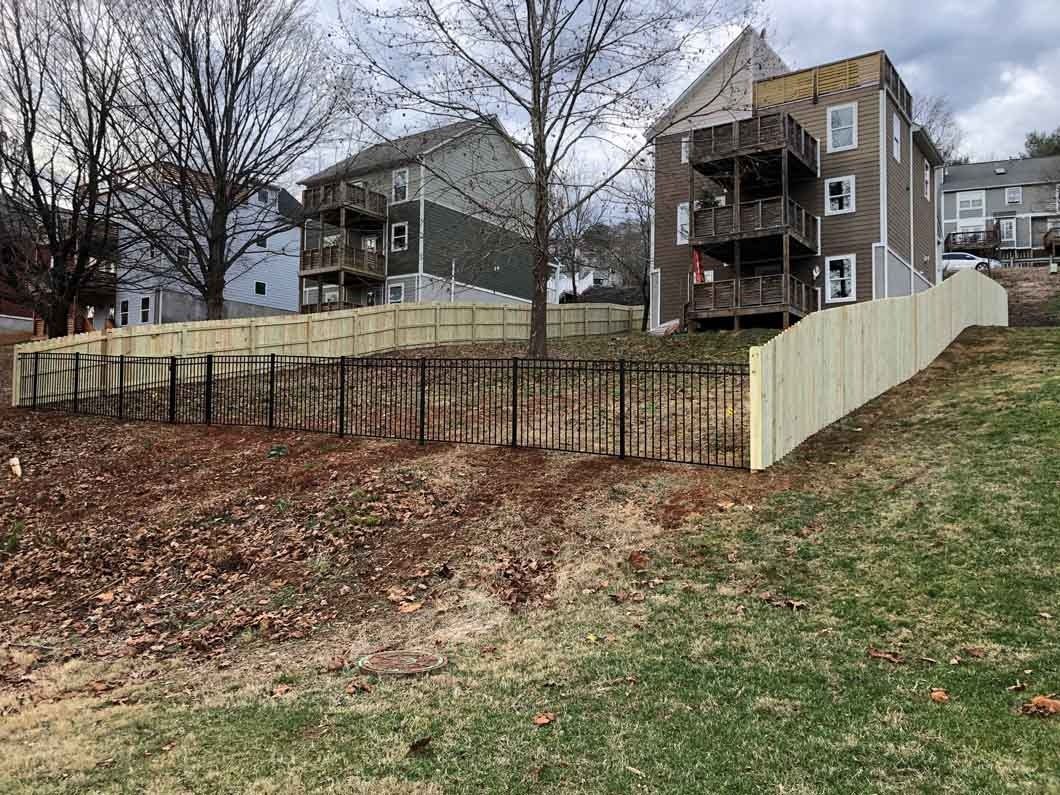 Fences around hillside with multi-story buildings in the background. Brown and green landscape.