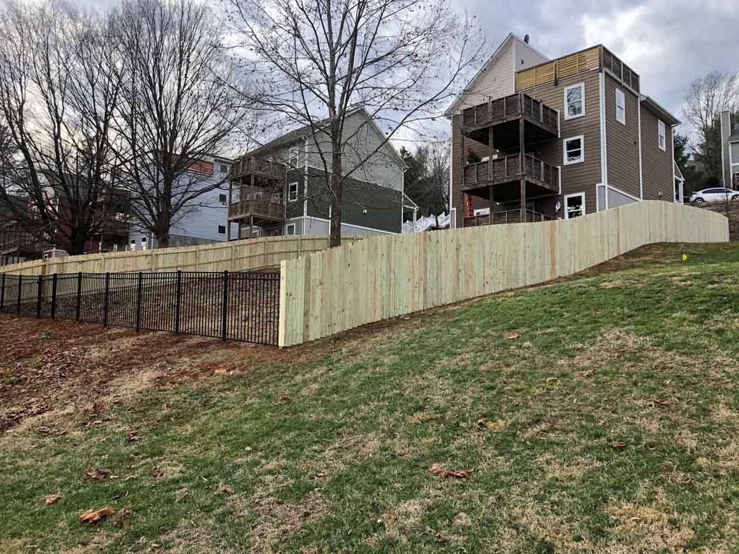 Wooden fence on a grassy hill, with houses and trees in the background.