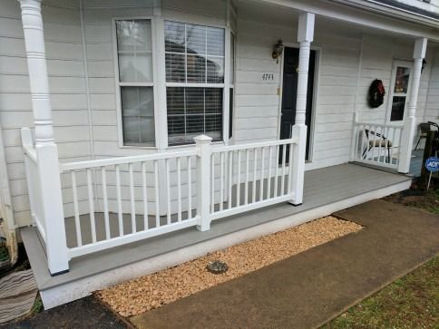 White porch with railing and columns, gray deck, window, front door. Tan gravel border along sidewalk.
