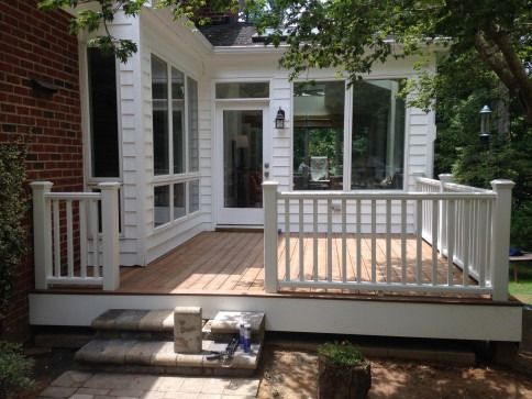 White deck and railing attached to a white sunroom with large windows, brick exterior, and stone steps.