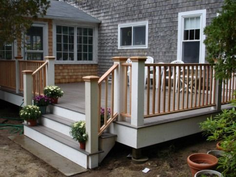 Deck with stairs, white posts, tan railing, potted flowers, and gray siding on a house.