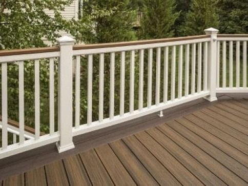 White railing with vertical balusters on a composite deck, brown wood deck, with trees in the background.