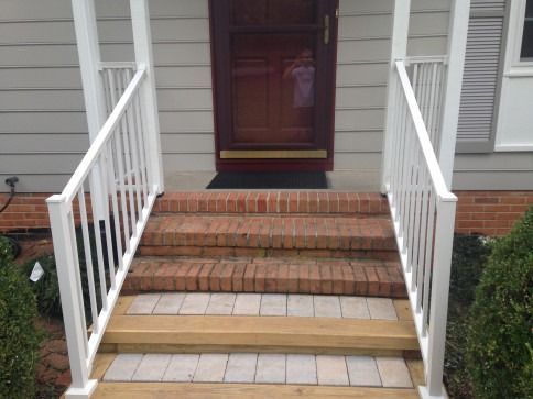 White-railed porch steps leading to a red door. Brick and tile steps, green bushes on sides.
