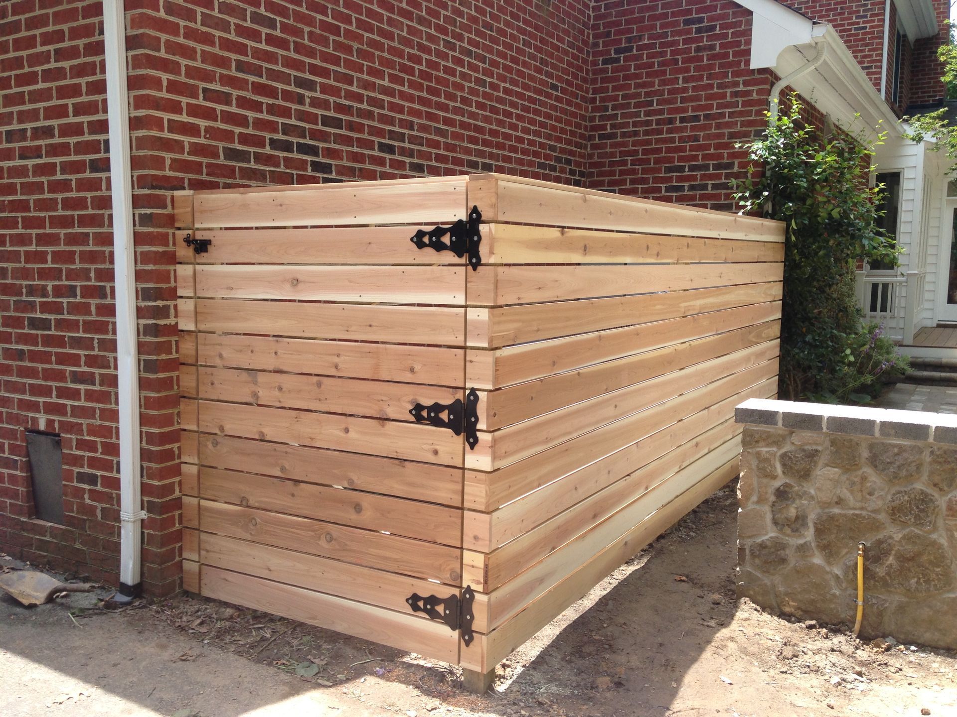 Wooden horizontal slat enclosure with black hinges against a brick wall.