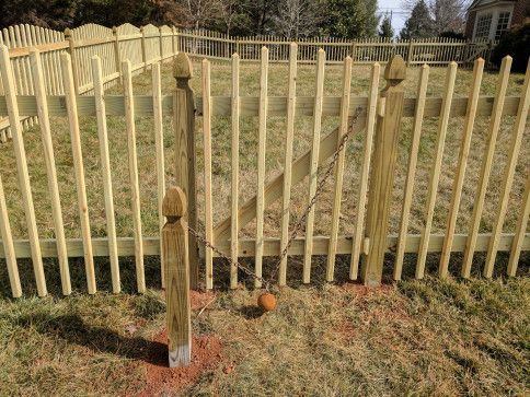 Wooden picket fence with a gate chained shut on a grassy lawn.