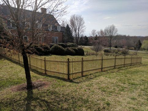 Wooden picket fence surrounding a house on a grassy lawn.