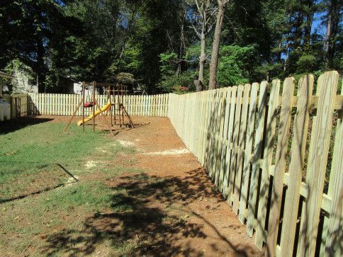 Wooden picket fence surrounding a backyard with a playground, trees, and grass.