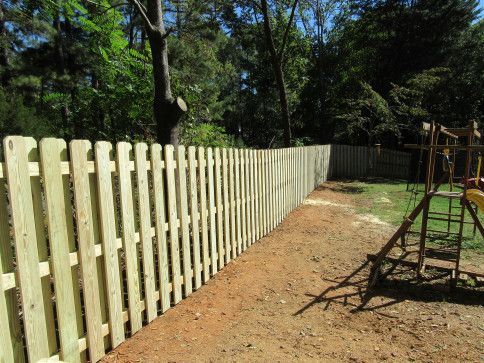 Light wooden picket fence bordering a yard with playground equipment and trees.