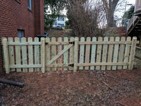 Wooden picket fence with a gate, next to a brick building.