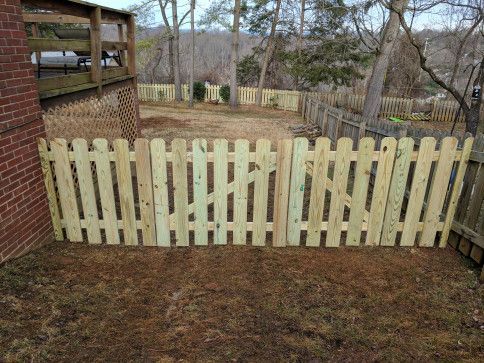 Wooden picket fence in a yard, connected to a brick building and a wooden deck.