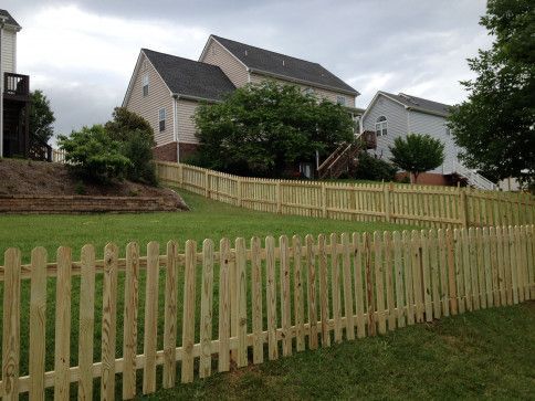 Wooden picket fence in a grassy yard, with houses in the background on a cloudy day.