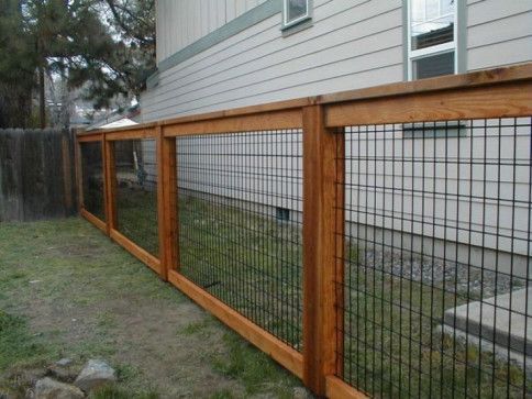 Wooden fence with black wire mesh panels alongside a house on a grassy lawn.