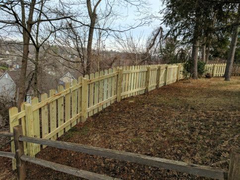 Wooden picket fence on a grassy hill, leading towards trees and a distant view.