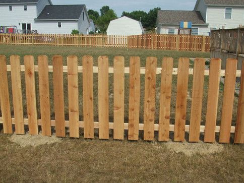 Wooden picket fence in a backyard, with houses and a white shed in the background.