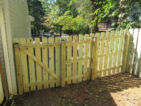 Wooden picket fence with a gate, in a yard with trees.