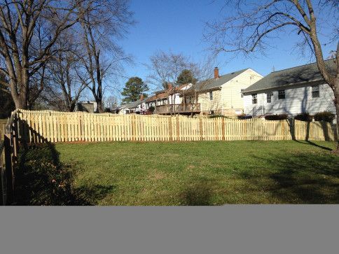 Wooden fence enclosing a grassy yard, with houses in the background on a sunny day.