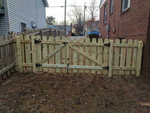 Wooden picket fence with double gate, in front of houses.