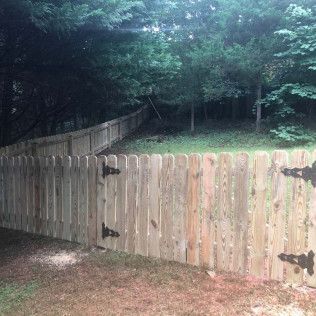 Wooden fence with black hinges, bordering a grassy area and trees.