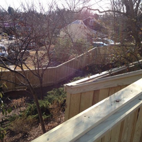 Wooden fence in a residential area, with trees and a house visible in the background. Sunny day.