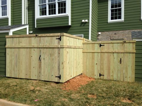 Two wooden enclosures against a green building, likely for trash or utilities.