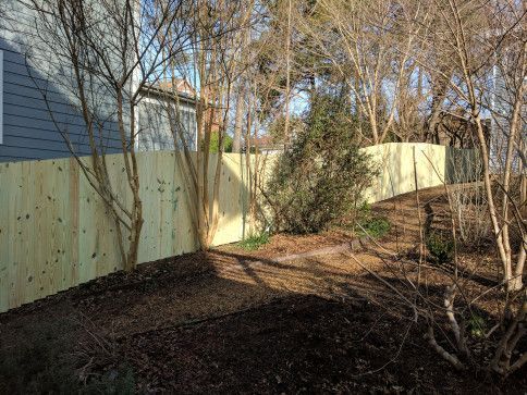 Wooden fence beside a building and bare trees in an outdoor setting.