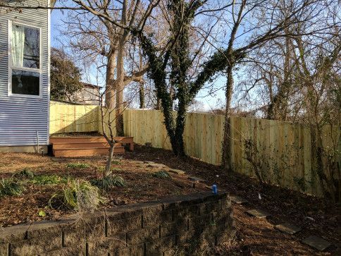 A new light wooden fence next to a yard with a brick retaining wall and a house.