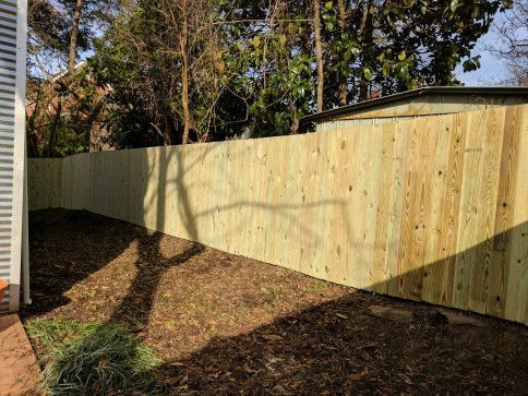 Wooden fence in a yard with leaves and a tree shadow.