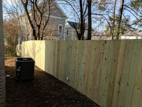 Wooden fence in a yard with an air conditioning unit and a house in the background.