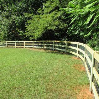A curved wooden fence encloses a green lawn, with trees in the background.