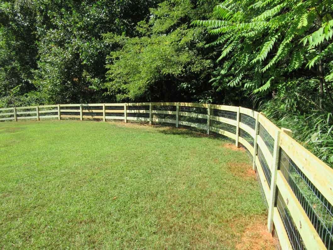 Green grassy area enclosed by a wooden fence, surrounded by trees.