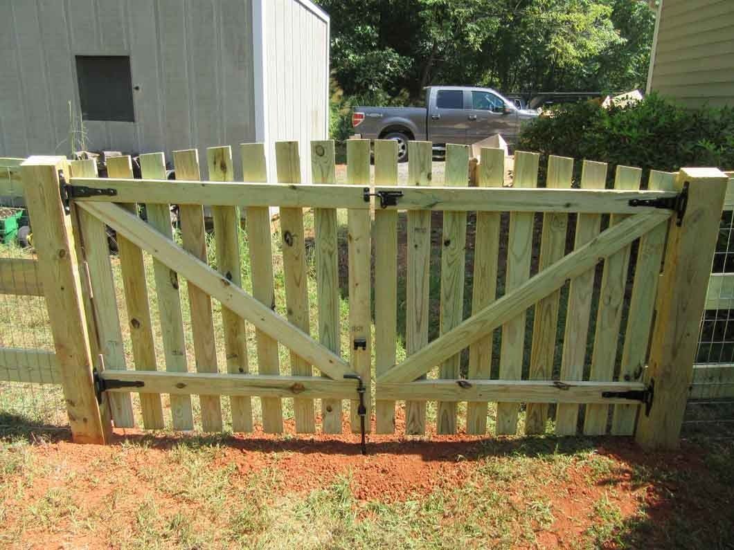 Wooden gate in a yard, light brown, with pointed top and diagonal bracing.