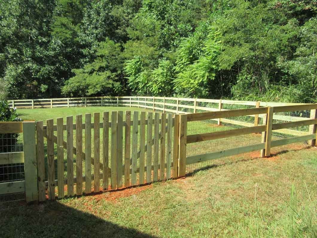 Wooden fence with gate in front of a green grassy area and trees.