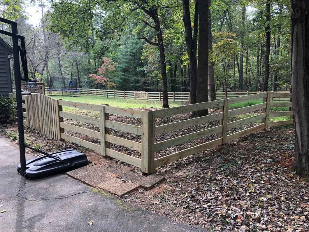 Wooden fence around grassy yard, basketball hoop, trees in the background.