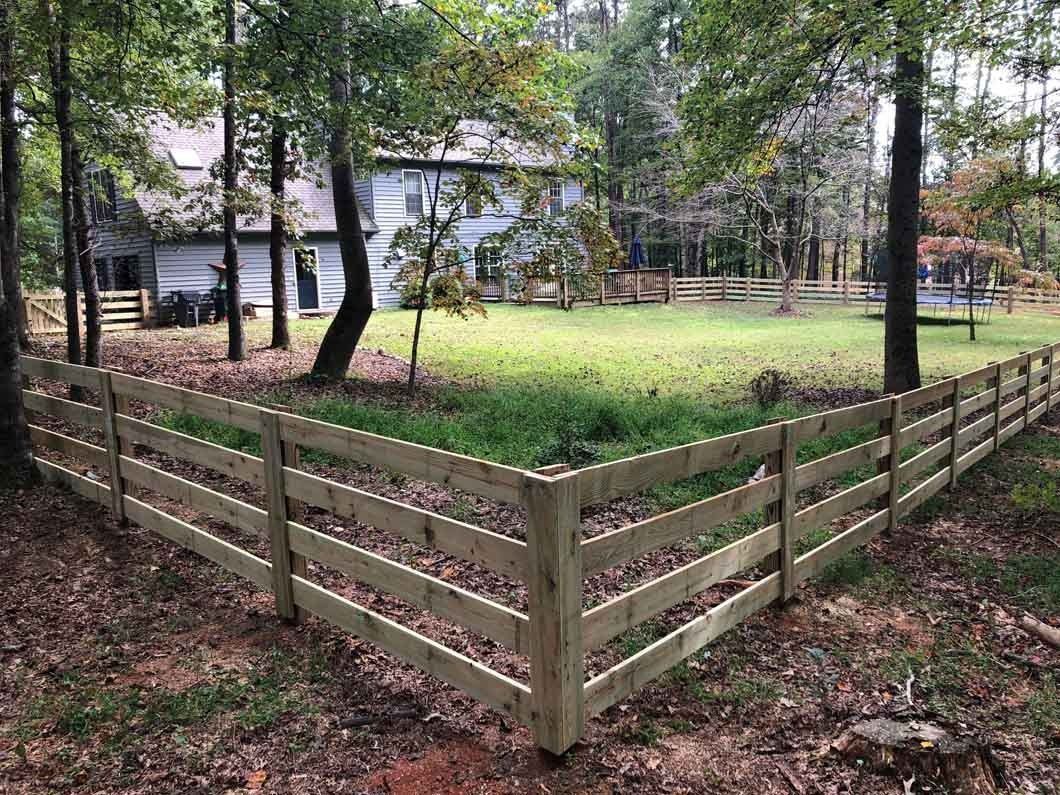 Wooden fence surrounds a yard with a house and trees in the background.