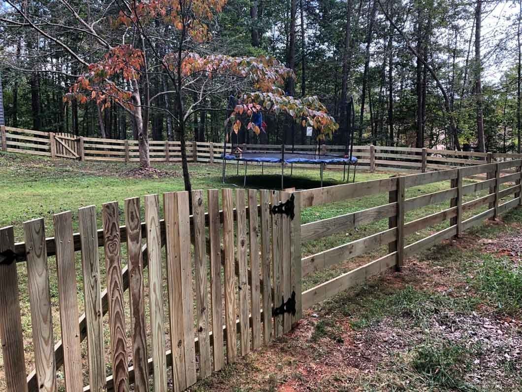 Wooden fence with gate, enclosing a backyard with trampoline and trees.